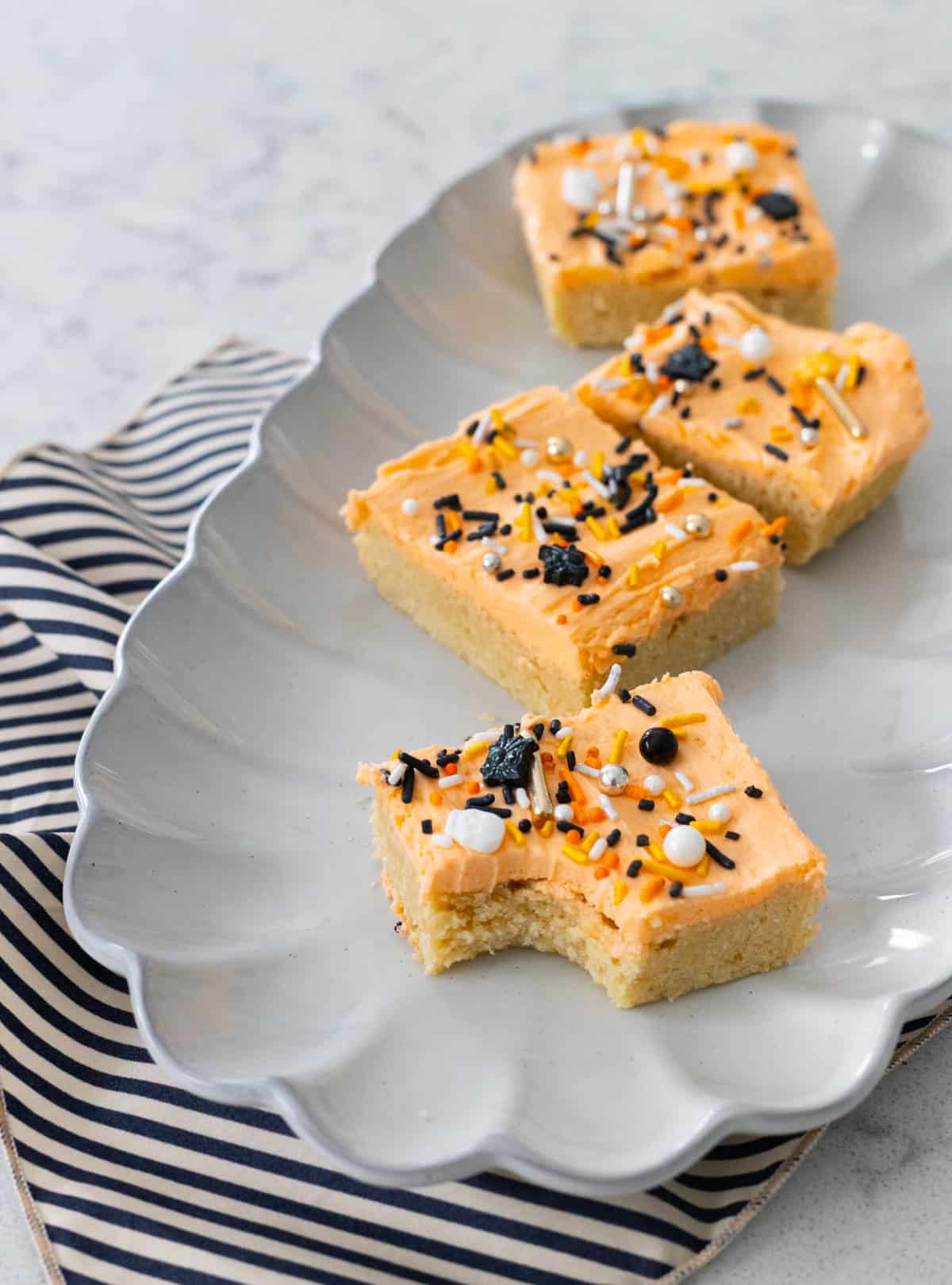 Une assiette grise a plusieurs barres de cookies d'Halloween carrées avec un glaçage orange et des paillettes effrayantes.
