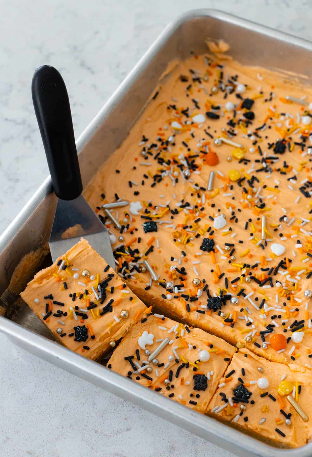 Les barres de cookies ont été glacées et décorées de paillettes. Une spatule soulève un carré pour servir.