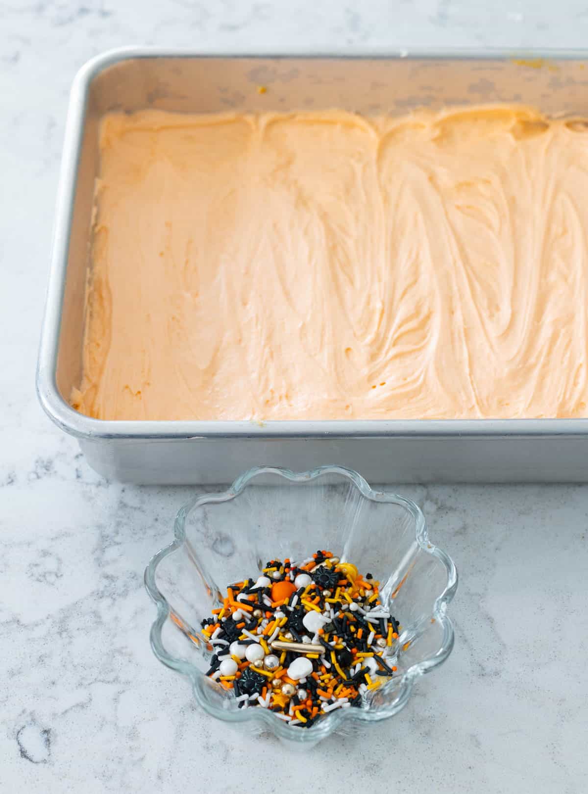 Le moule à cuire a été glacé avec un glaçage orange, un bol de paillettes est à côté.