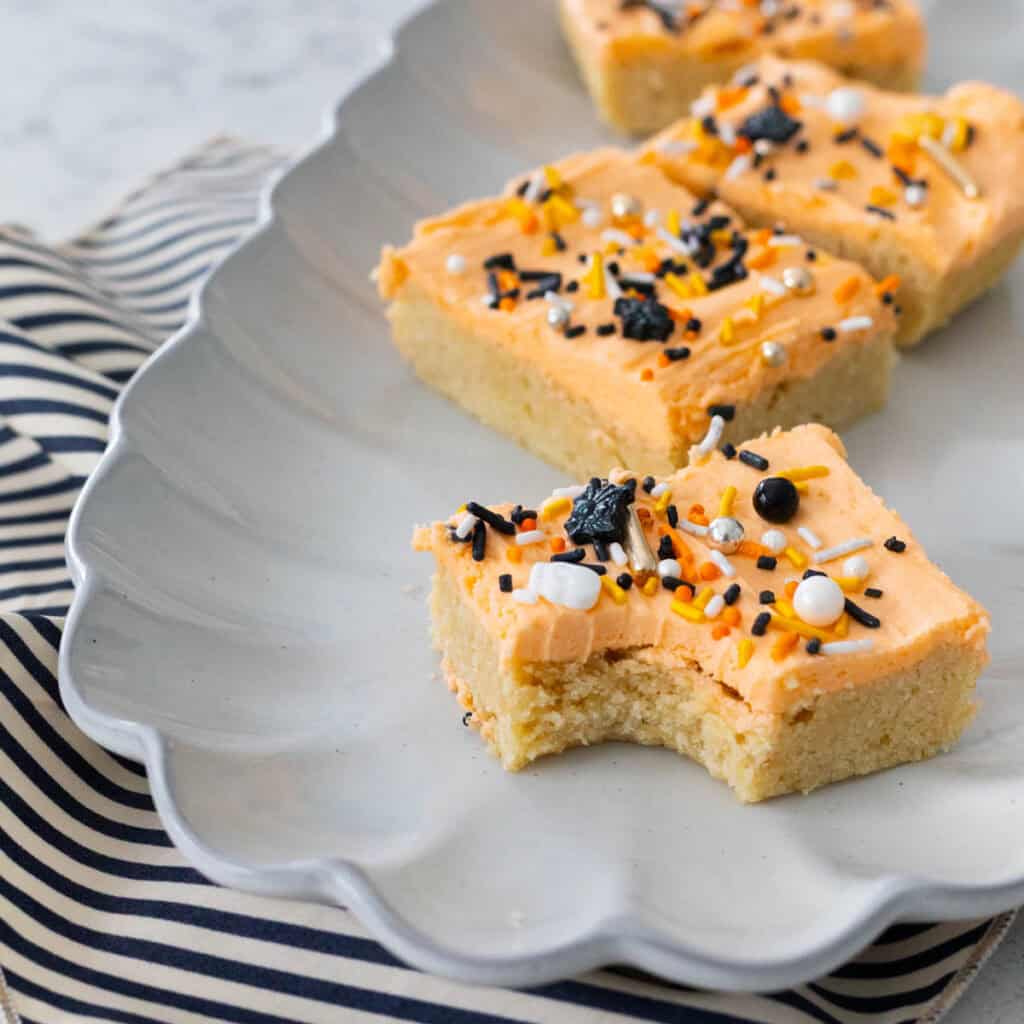 A grey platter has several square Halloween cookie bars with orange frosting and spooky sprinkles.