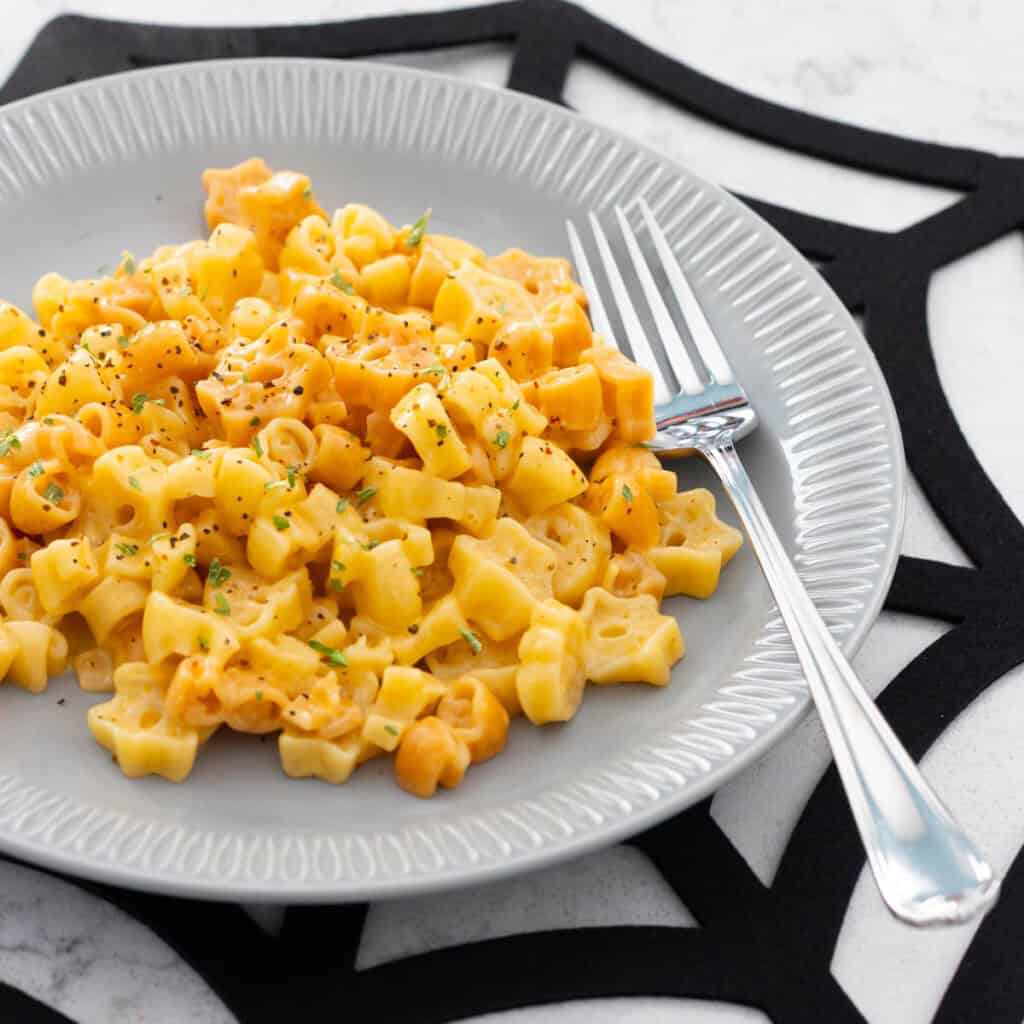 A grey plate has Halloween pasta scooped on top, the plate rests on a spiderweb place mat.