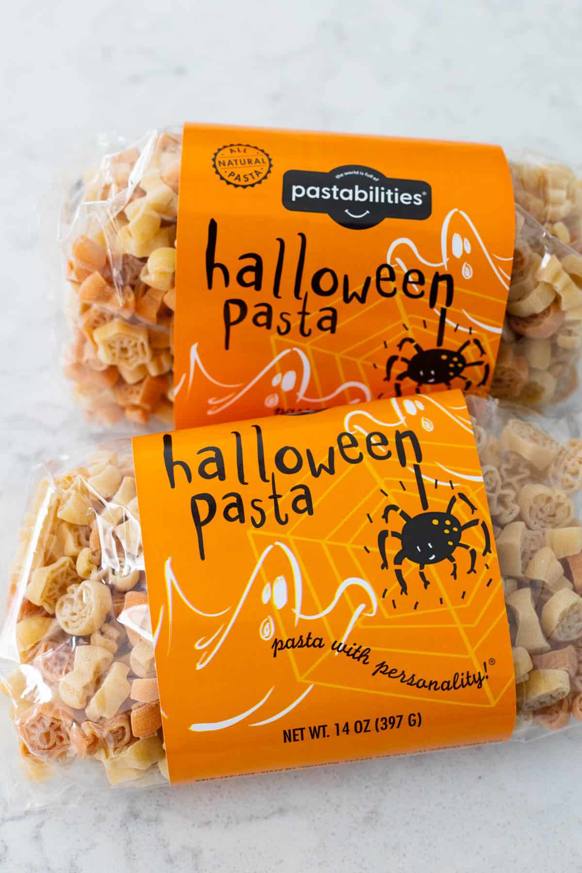 Two bags of Halloween shaped pasta are ready to be cooked for dinner. The shapes include spider webs and ghosts.