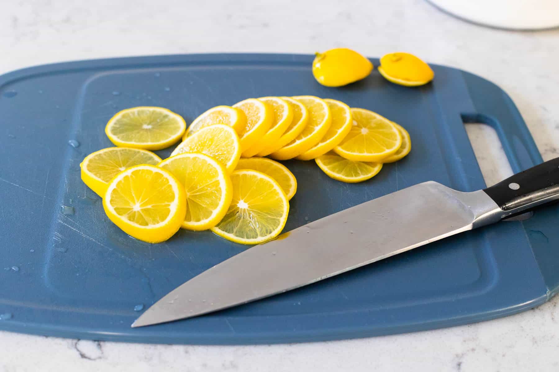 Des rondelles de citron Meyer finement tranchées sont disposées sur une planche à découper à côté d'un couteau de cuisine, prêtes à être utilisées pour faire du limoncello.