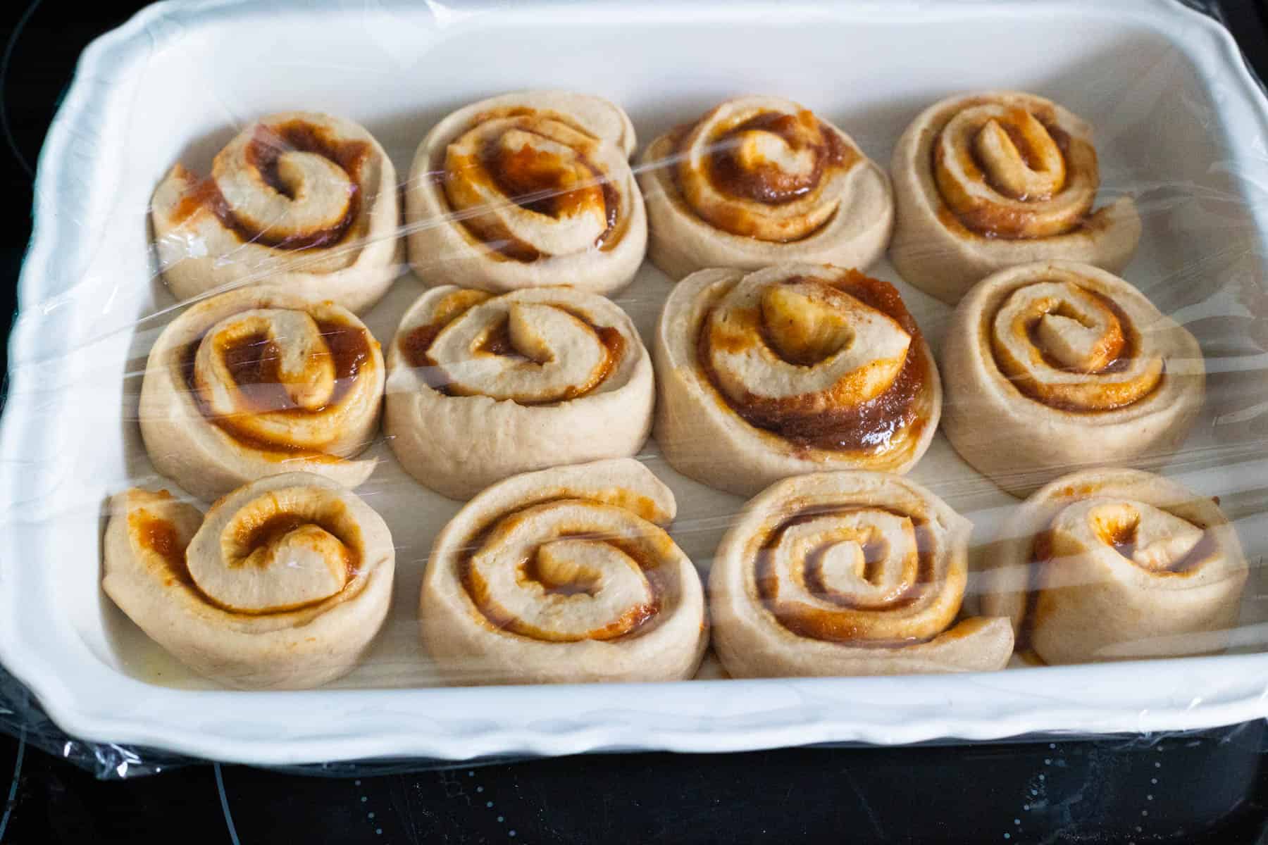 The baking dish filled with cinnamon rolls is covered in plastic wrap.