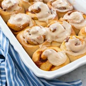 A baking pan filled with pumpkin spice cinnamon rolls with browned butter icing.