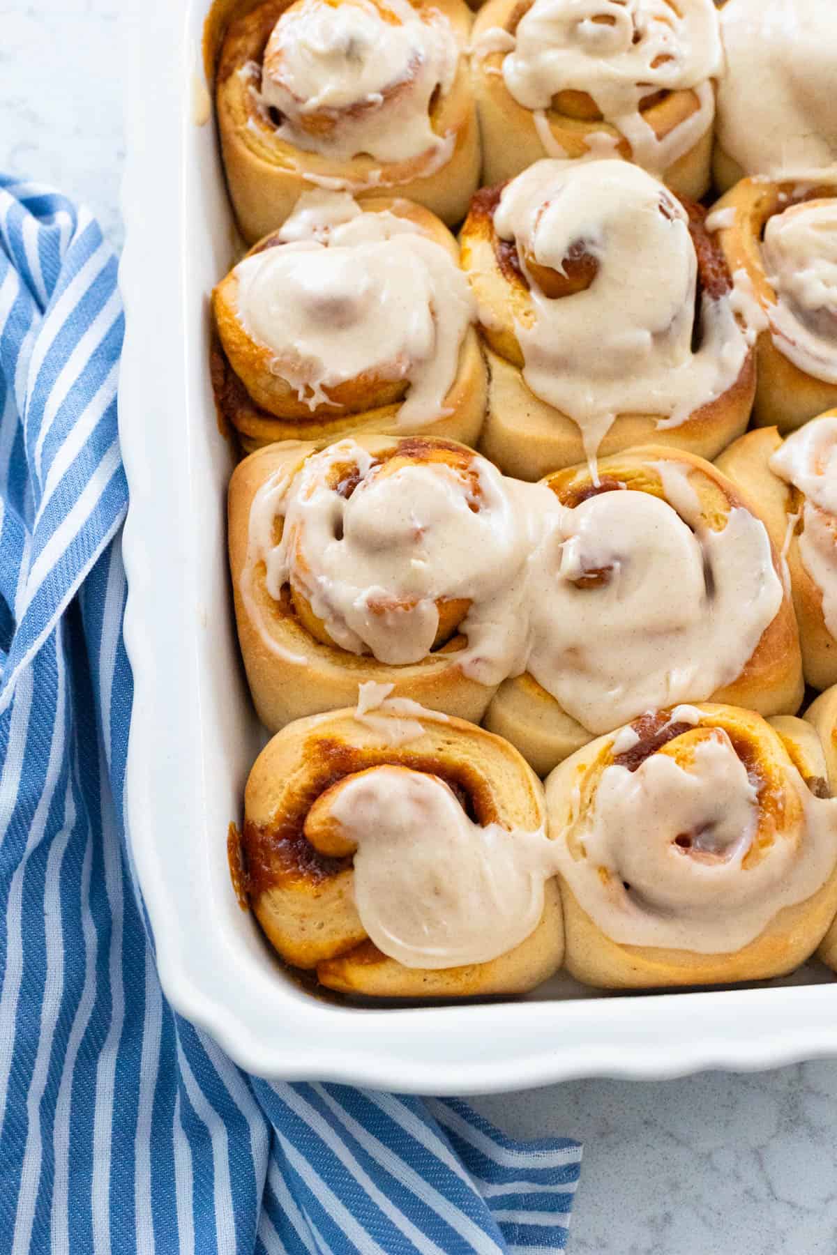 A baking pan filled with pumpkin spice cinnamon rolls with browned butter icing.