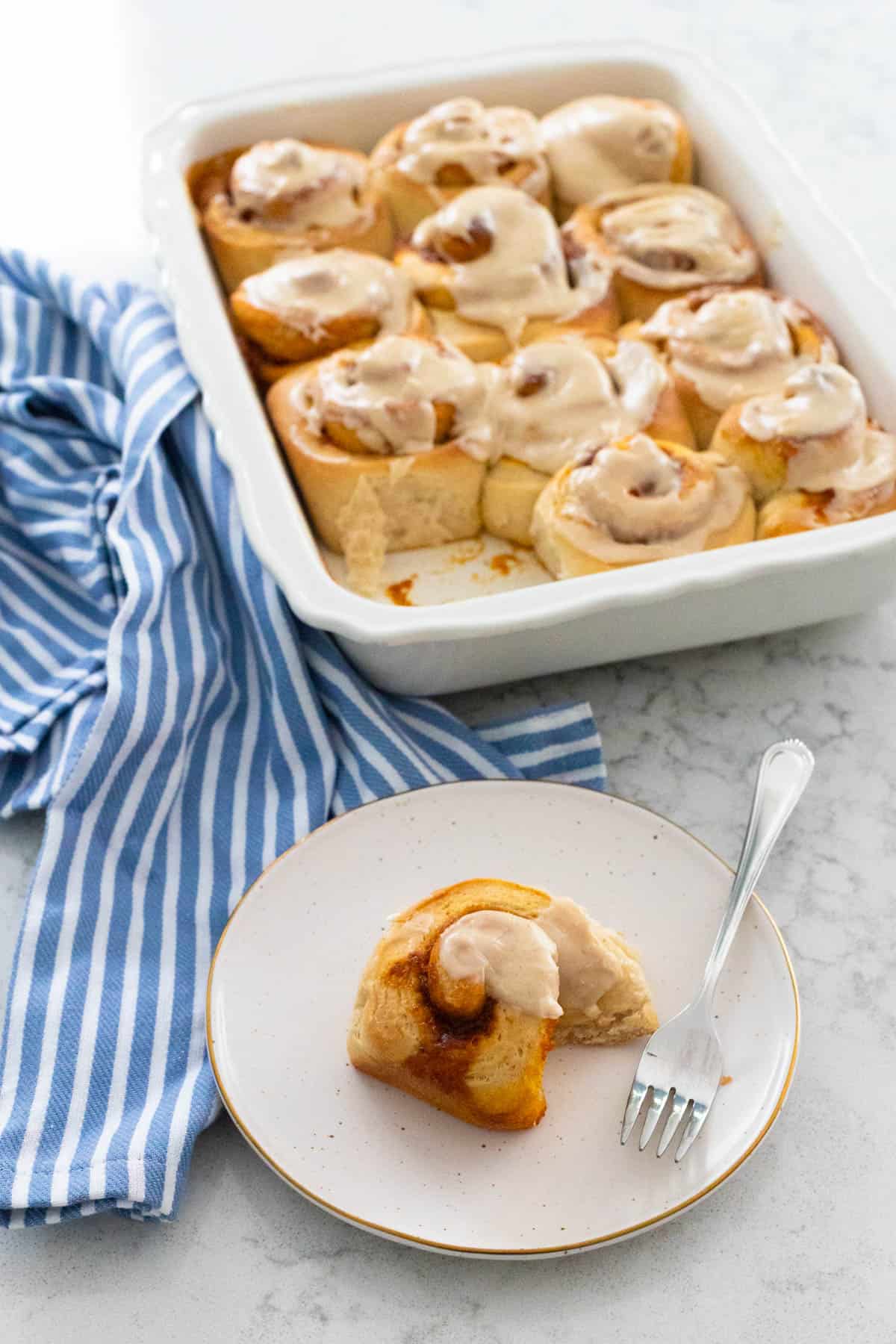 A pumpkin cinnamon roll with browned butter glaze has been served up on a plate, a fork nearby has just taken off a bite.