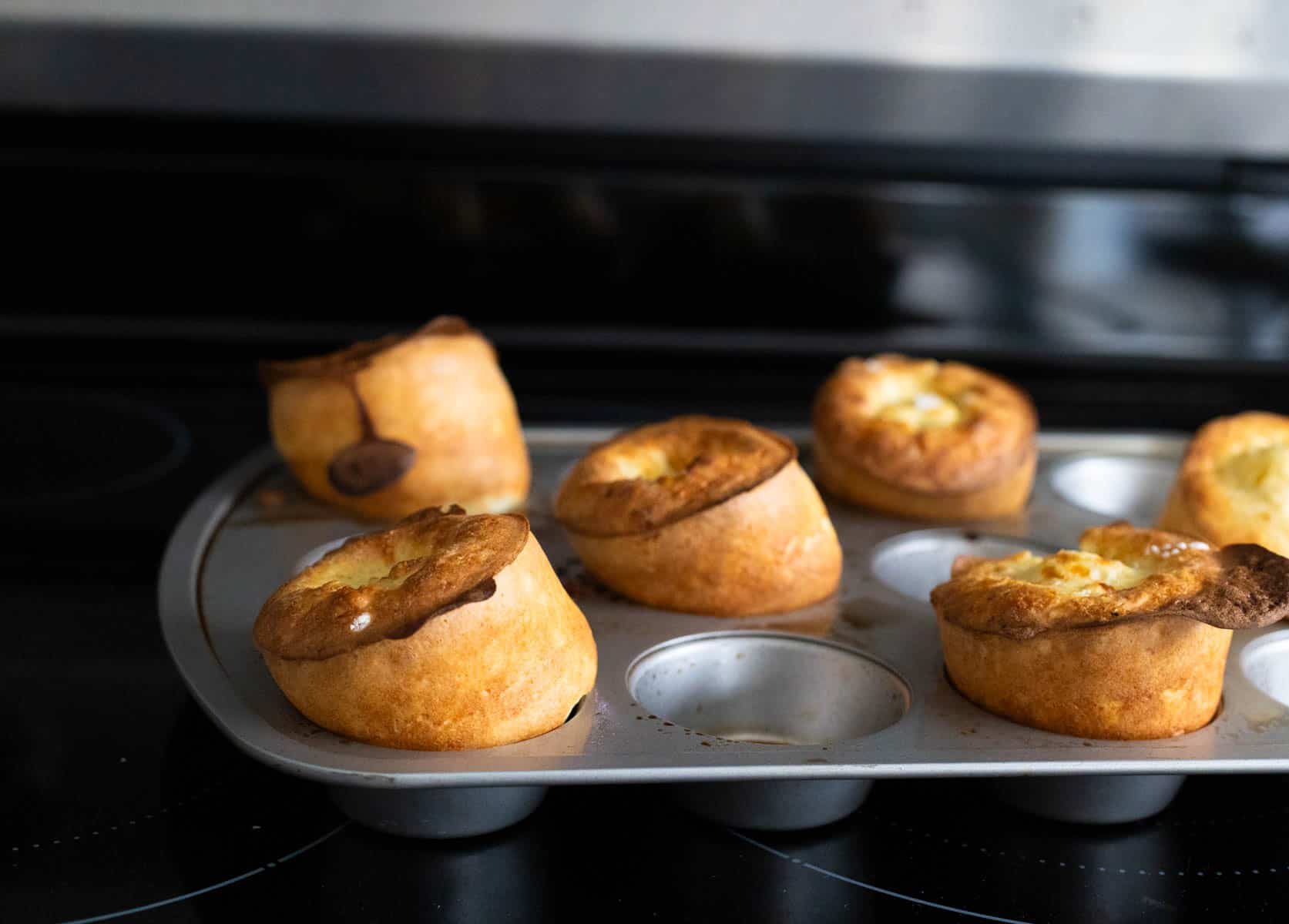 The popovers are fresh from the oven and have puffed up over the top of the muffin tin where they were baked.