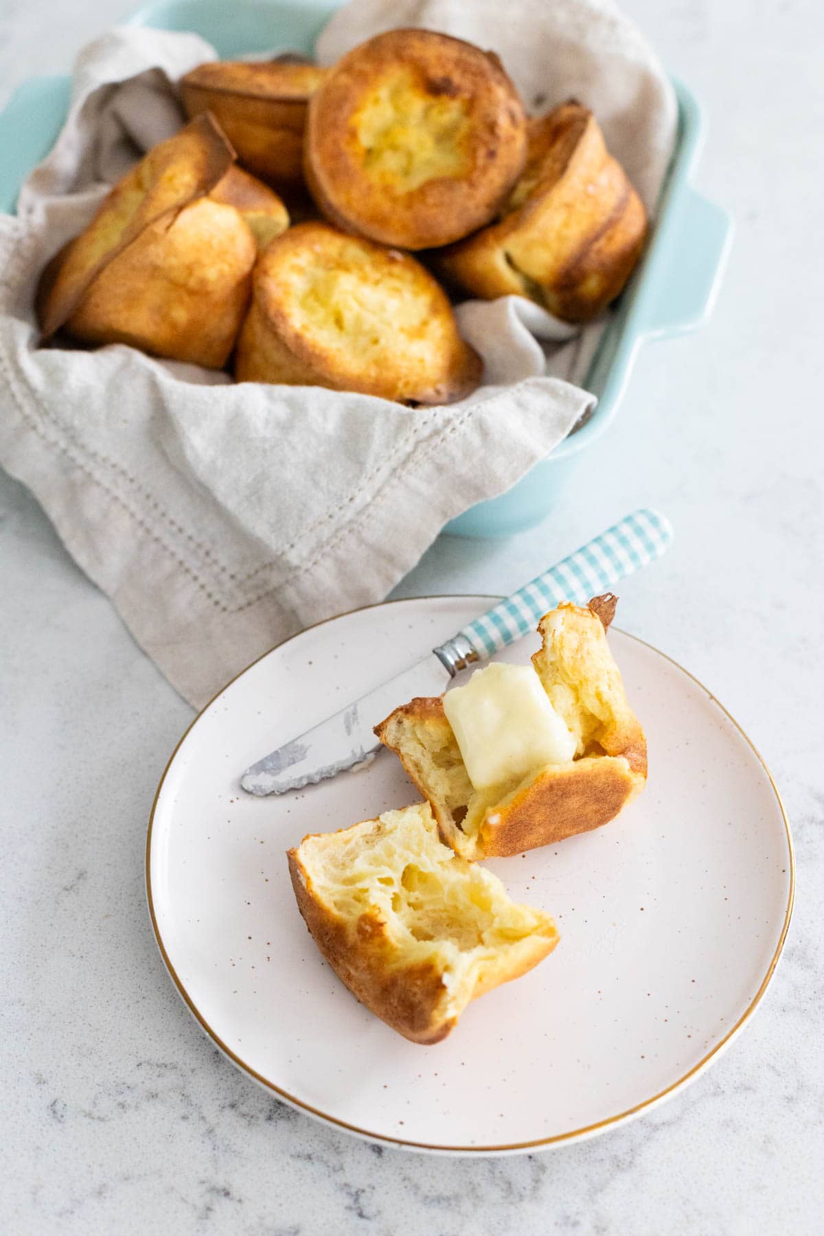 The basket of sourdough popovers have been served, one of the popovers is on a small plate and split open with a pat of butter melting on top.