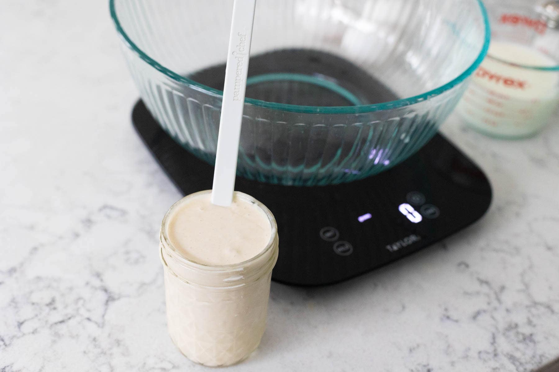 The sourdough discard is in a mason jar in front of a measuring bowl sitting on a food scale.