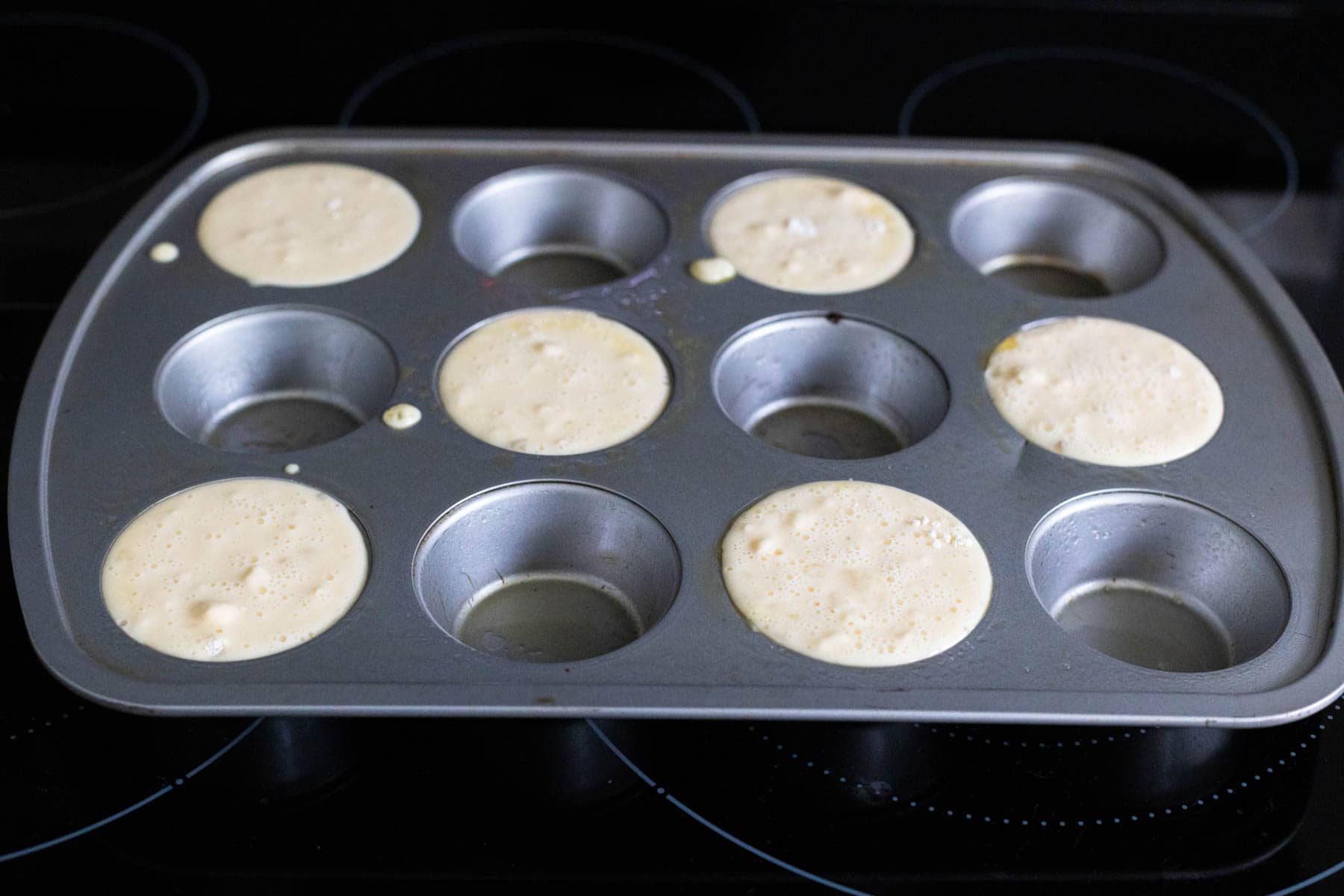 The popover batter has been poured into a hot muffin tin with an open space between each well.