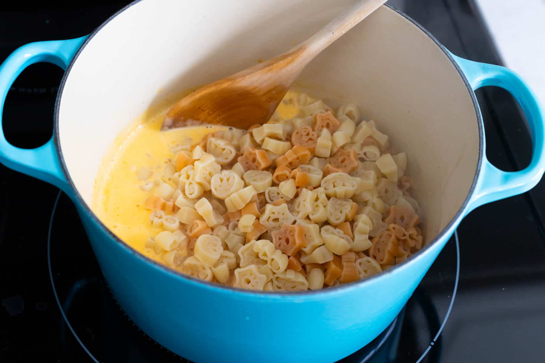 The pasta has been added to the cheese sauce in the pot.