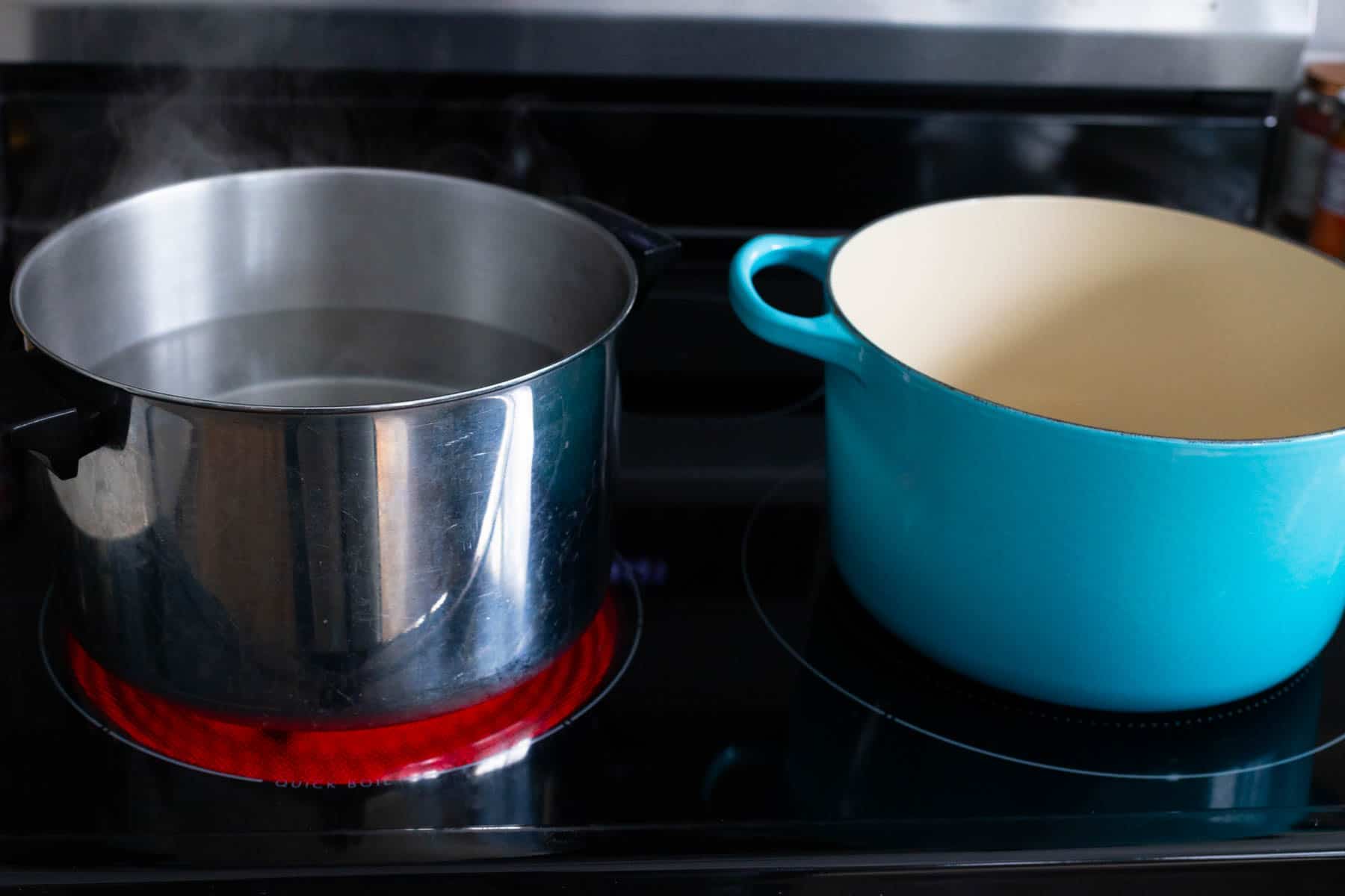 A pasta pot next to a sauce pot on the stovetop.
