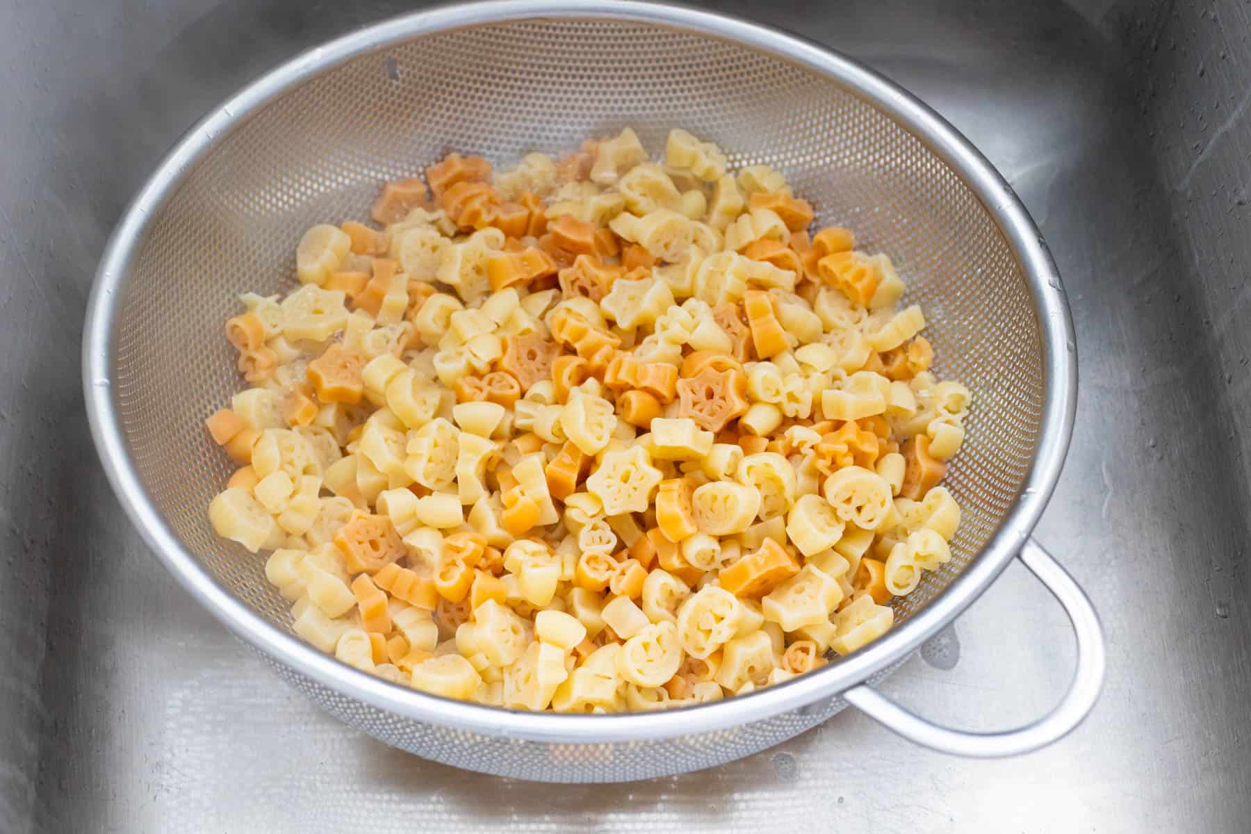 The Halloween shaped noodles have been drained into a strainer in the sink.