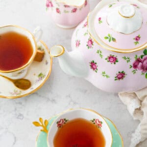 A tea party scene features two tea cups filled with freshly brewed tea and a pink flowered tea pot.