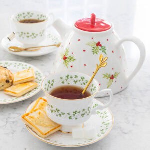 A Christmas tea pot next to two cups of tea.