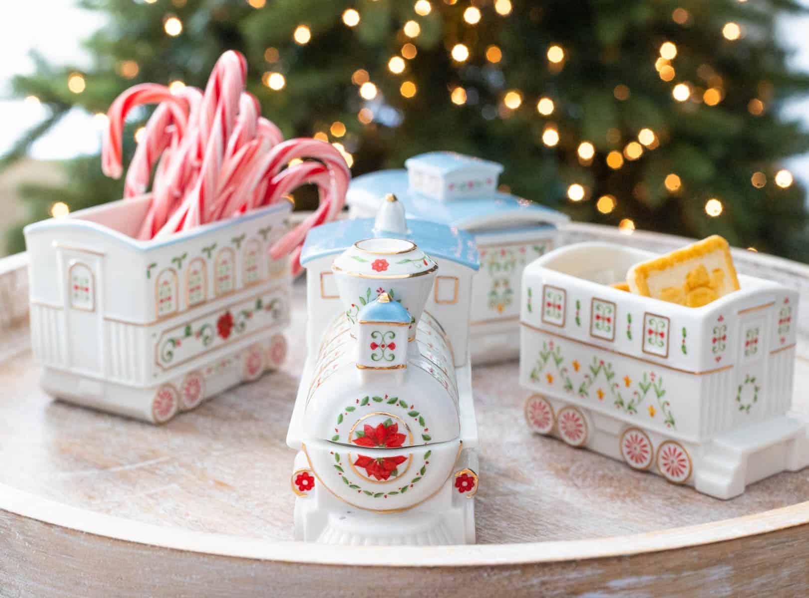The train serving piece by Lenox is filled with candy canes and cookies and has been arranged in front of a Christmas tree.
