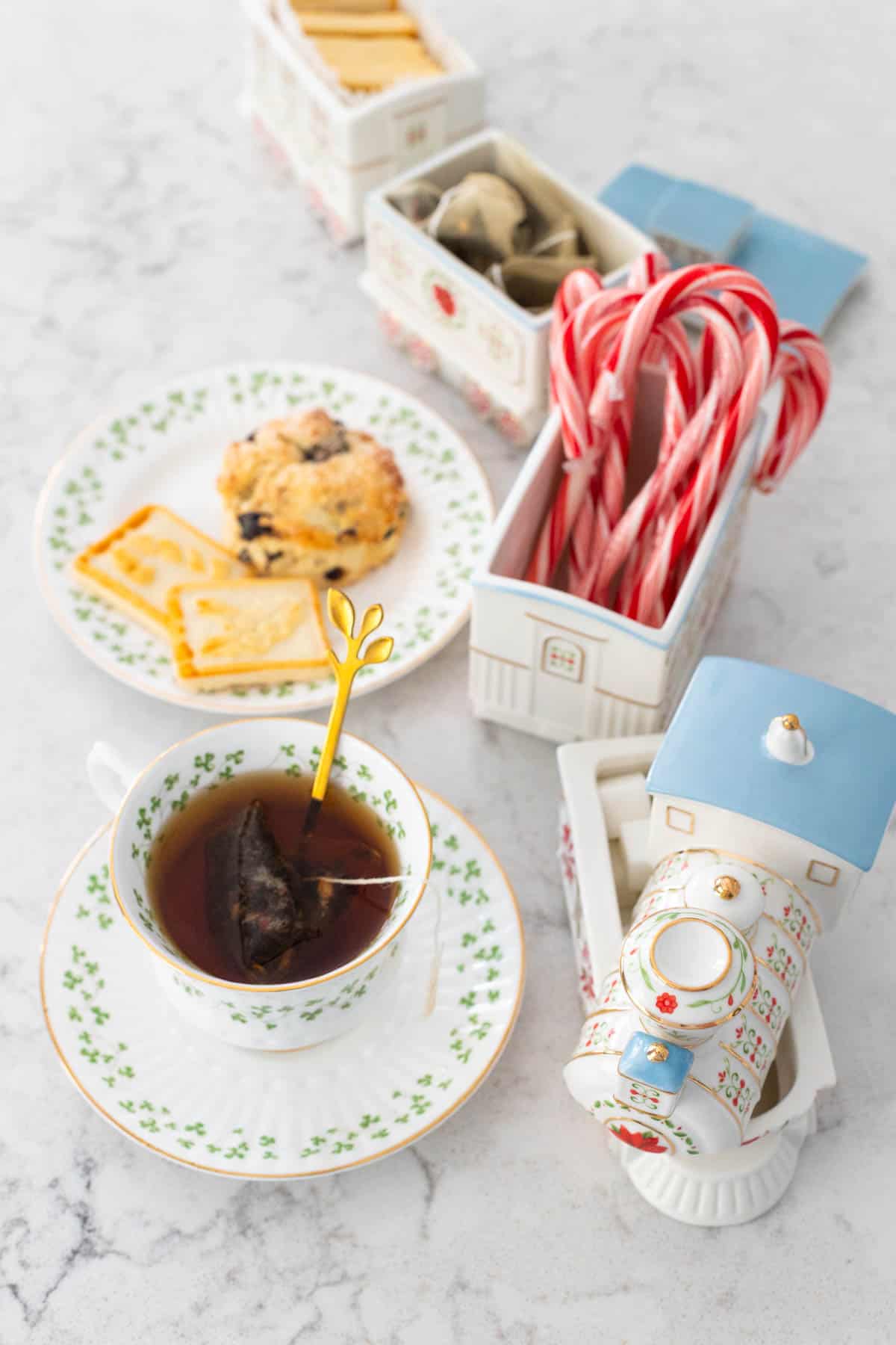 A cup of tea and a plate of scones and cookies sit next to a holiday Train serving piece.