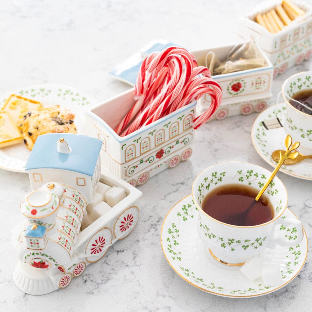 A Christmas train is filled with candy canes, shortbread cookies, and tea bags and sits next to a cup of tea.