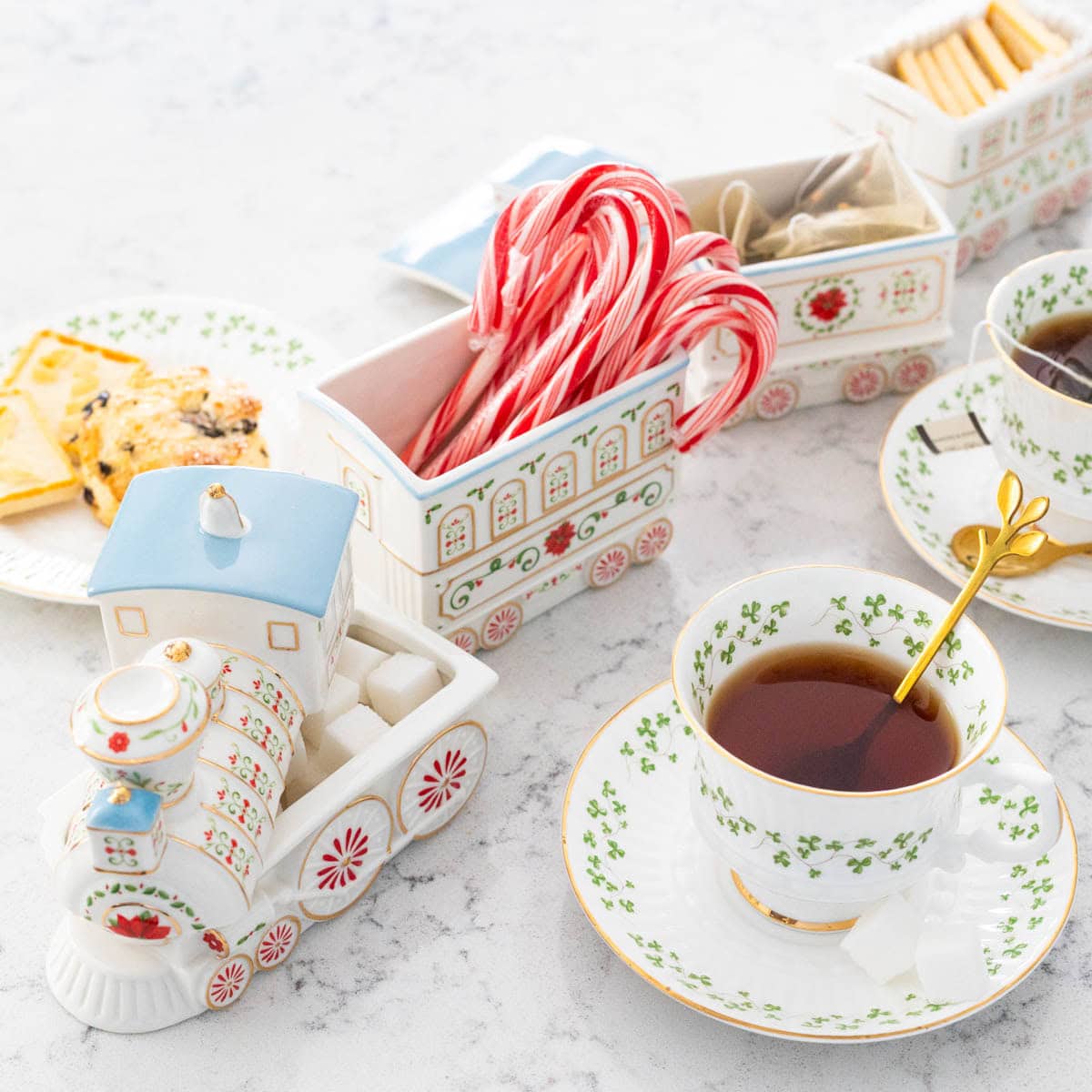 A Christmas train is filled with candy canes, shortbread cookies, and tea bags and sits next to a cup of tea.