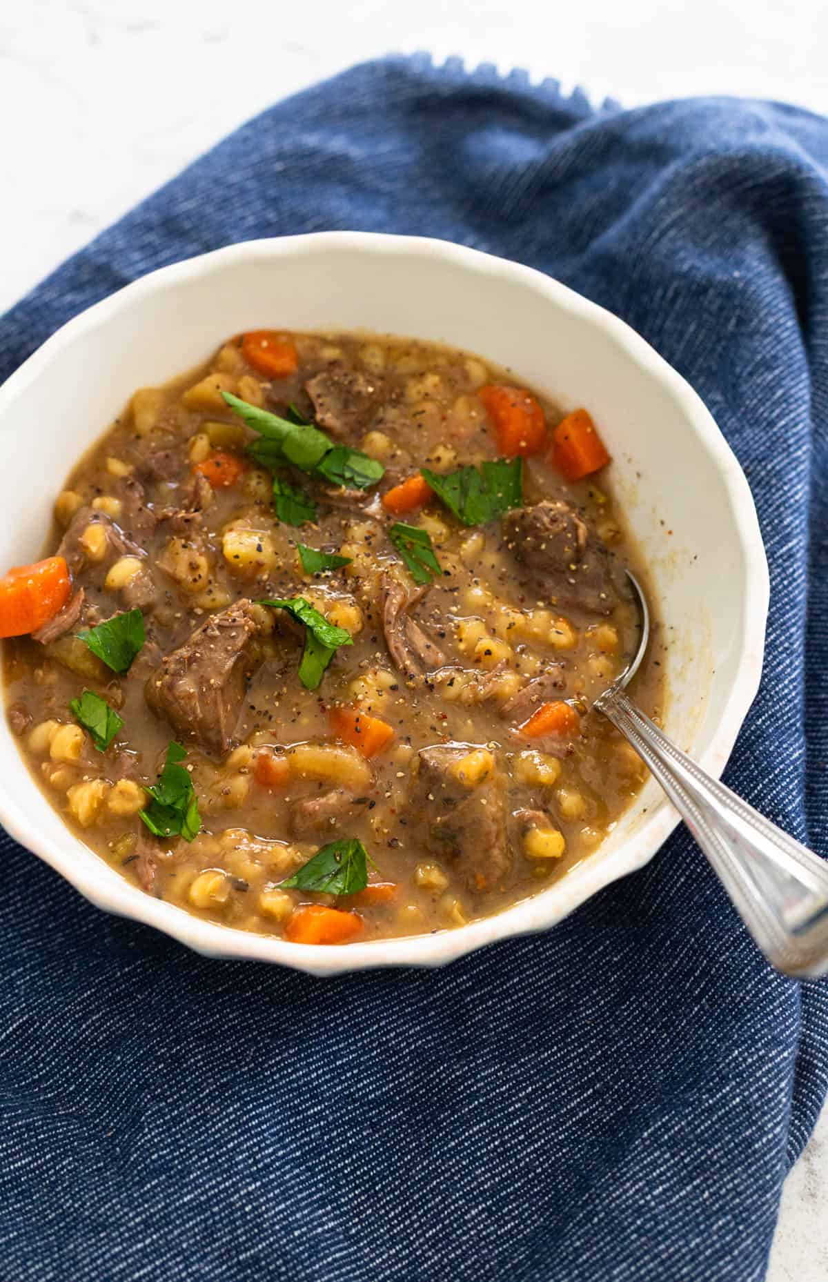 A bowl of thick, beefy stew with vegetables and barley is topped with fresh parsley.