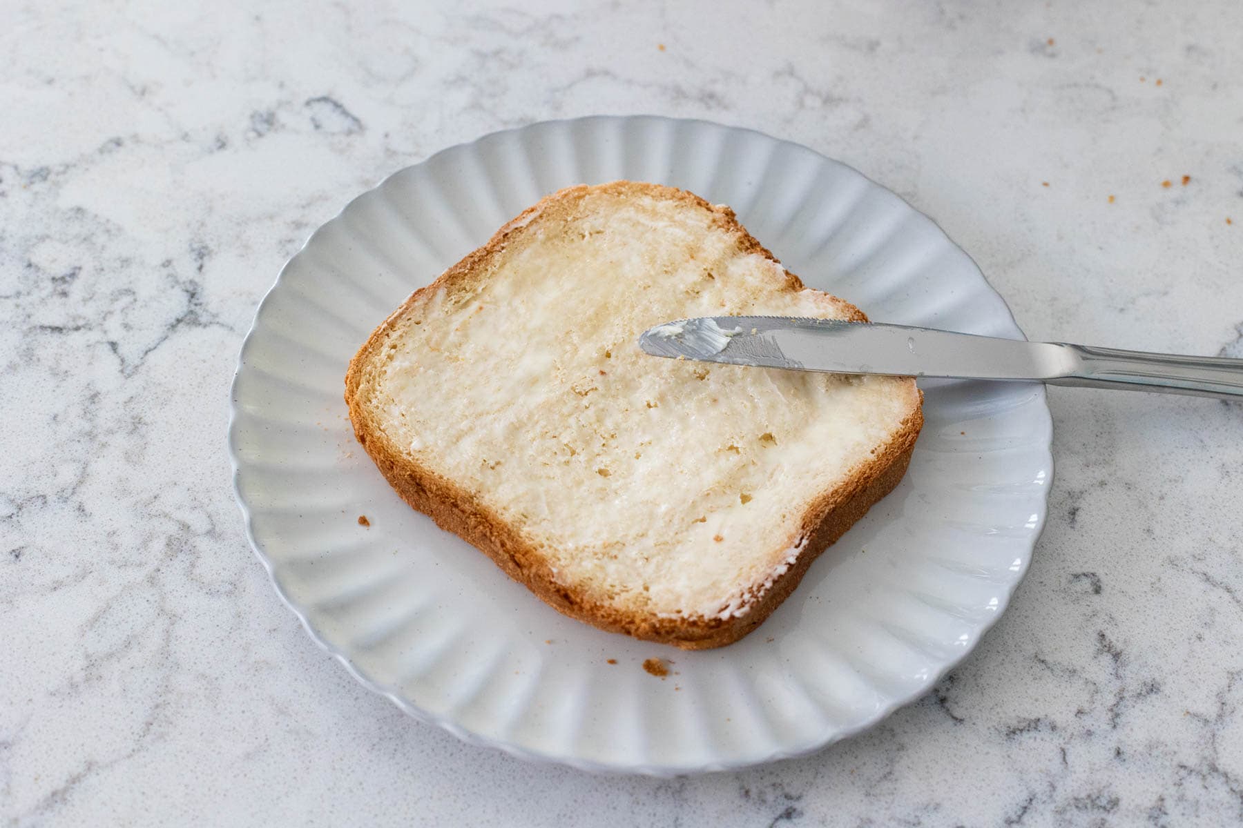Butter is being spread over the bread with a knife.