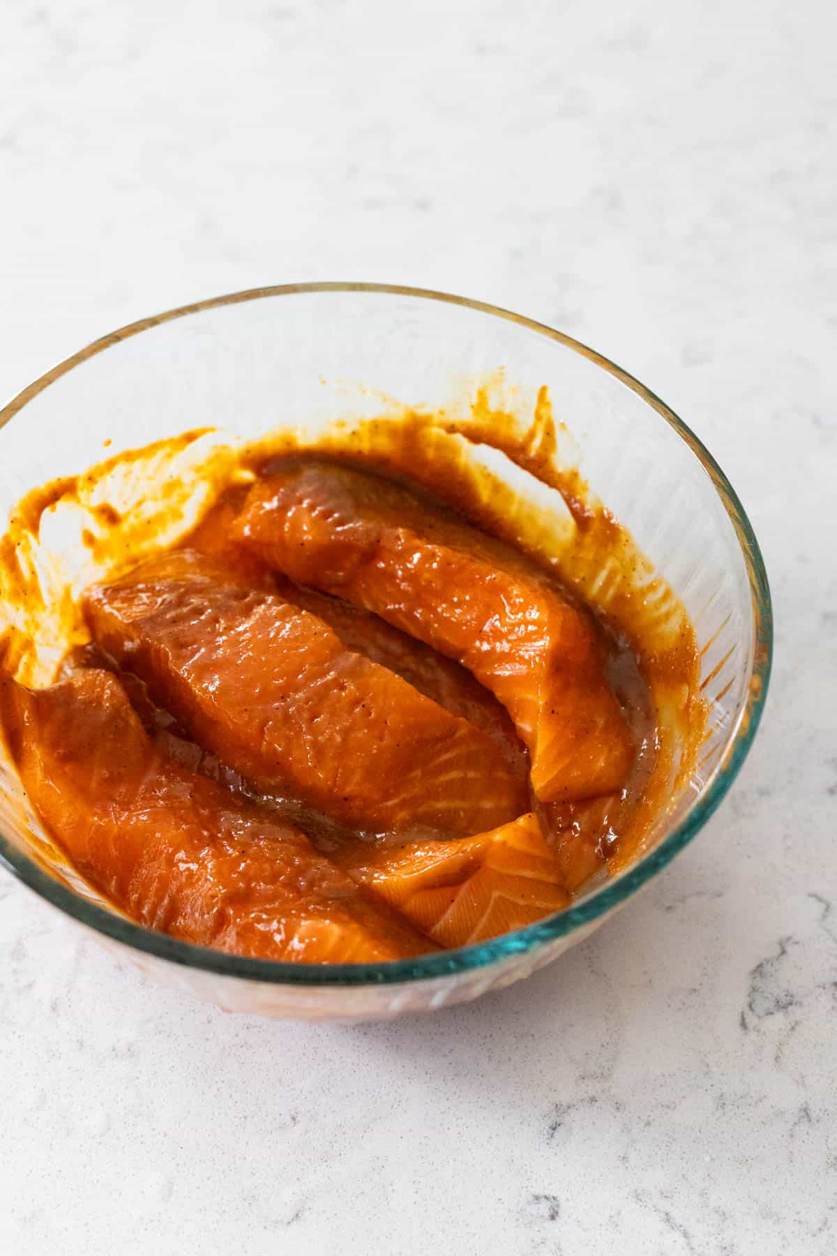 Fresh salmon fillets coated in a miso marinade inside a glass bowl.