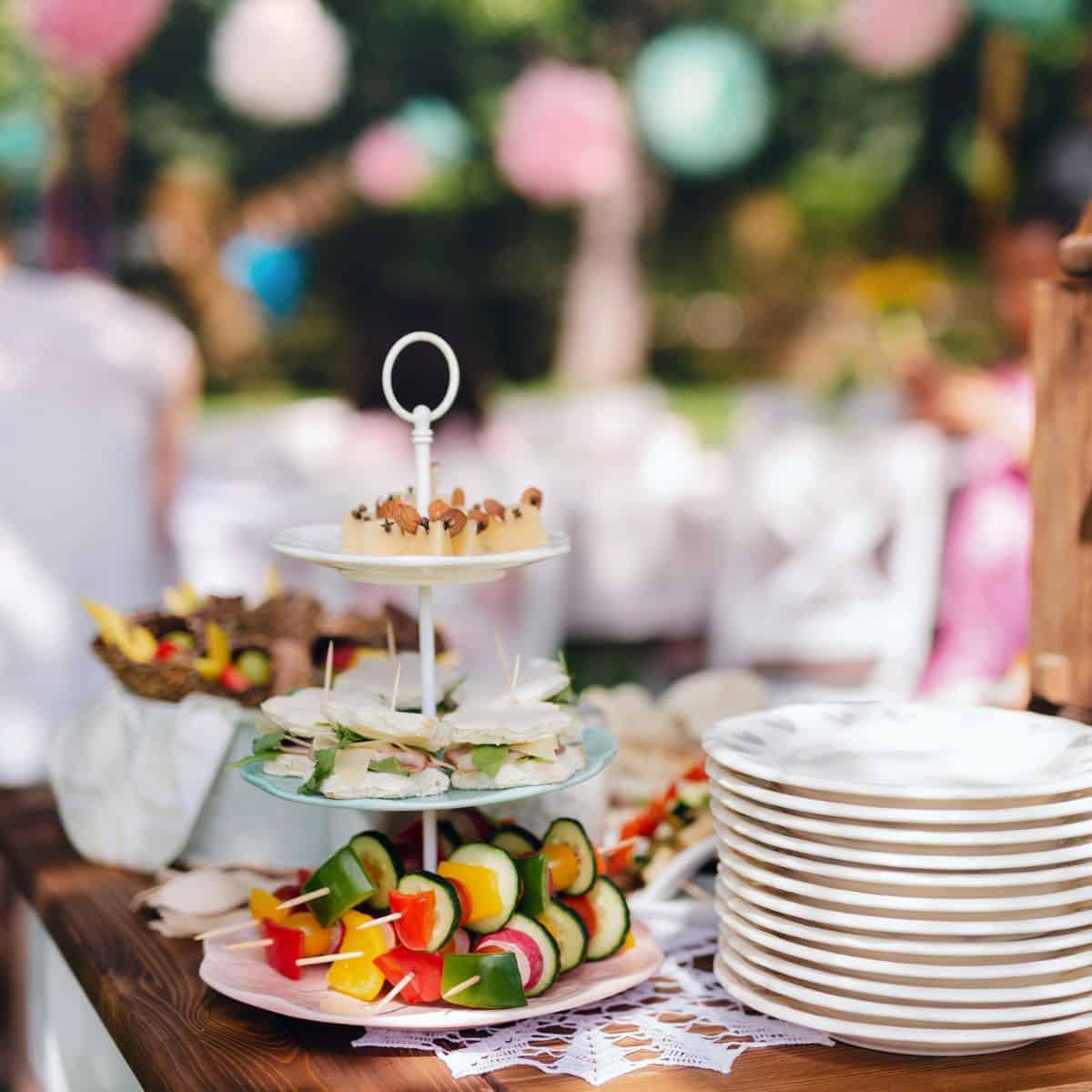 A tiered tray of appetizers sits next to a stack of party plates.