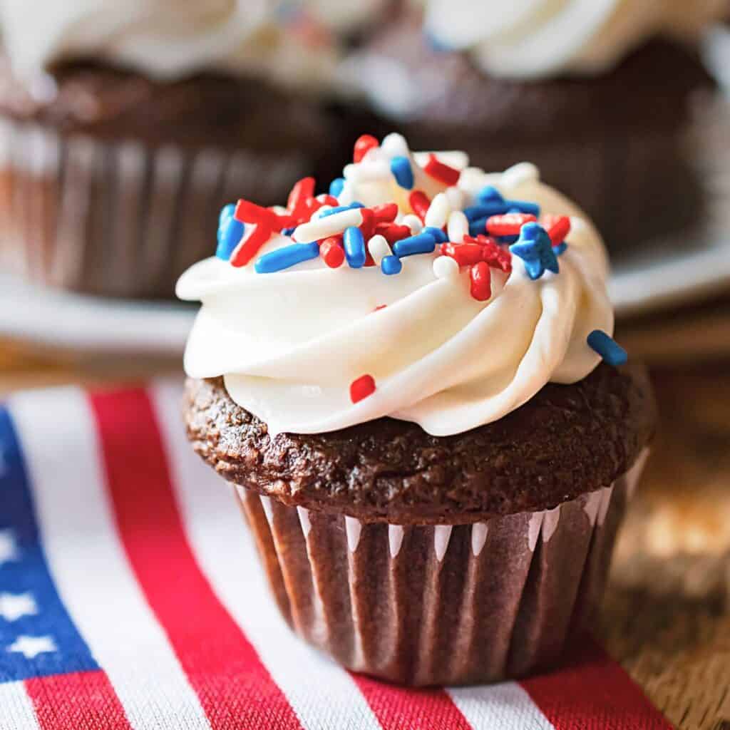 A chocolate cupcake with white frosting is decorated with red, white, and blue sprinkles.