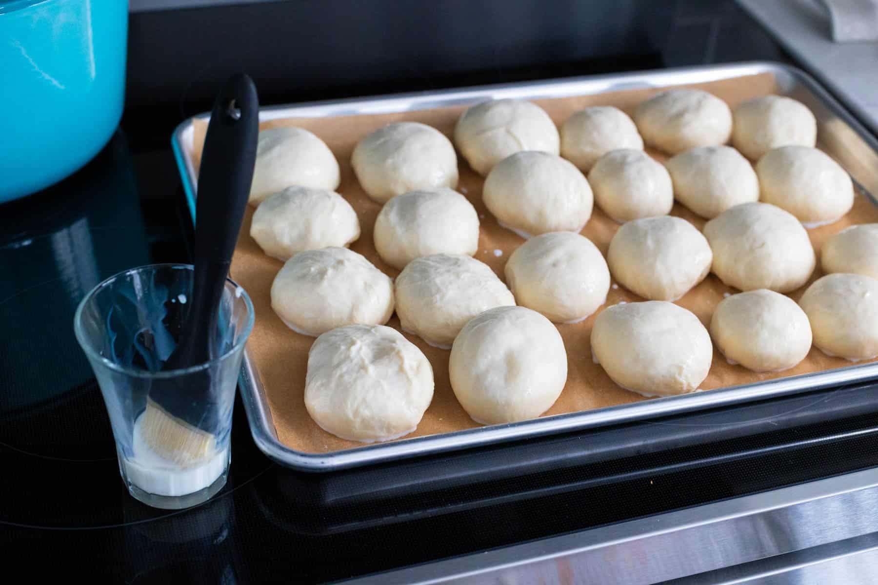 The cup of milk has a pastry brush ready to coat the buns.