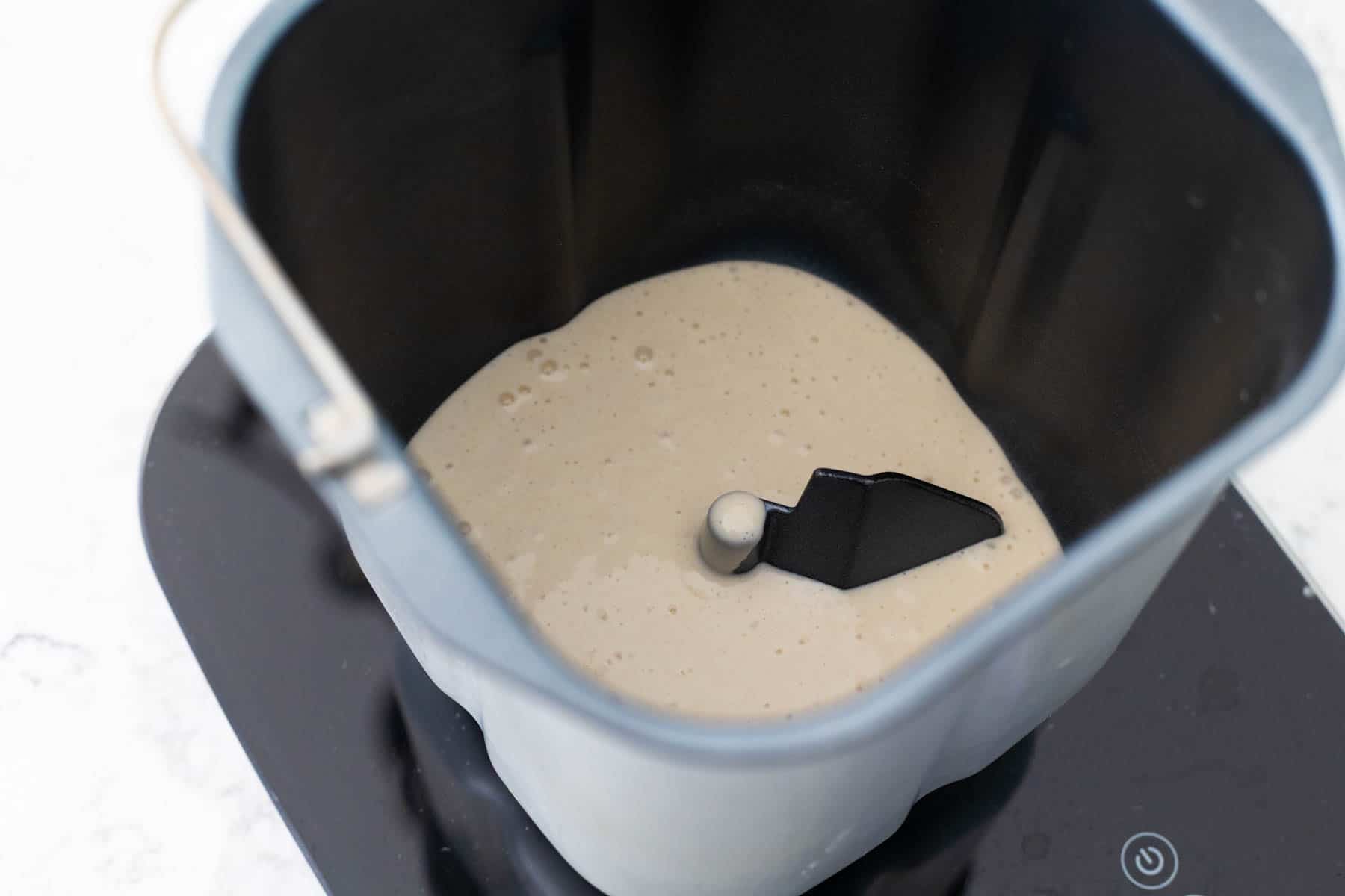 The sourdough starter has been added to the bread maker pan fitted with the paddle attachment.