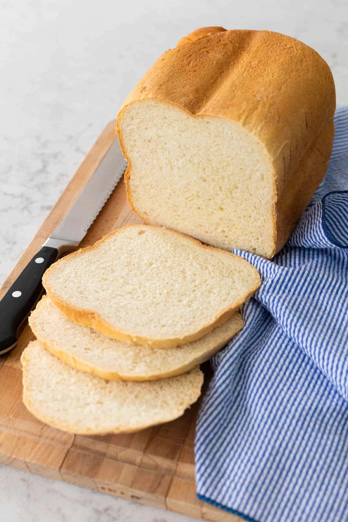 A loaf of sourdough white bread has been sliced on a cutting board with a blue striped napkin on the side.
