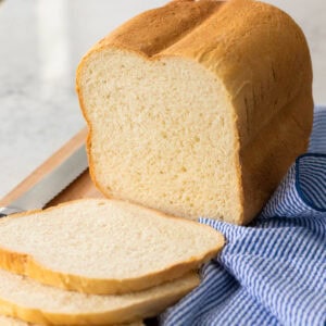 A loaf of sourdough white bread has been sliced on a cutting board with a blue striped napkin on the side.