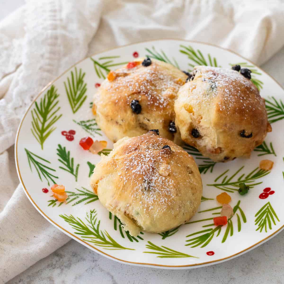 Three golden Stollen buns dusted with powdered sugar and studded with dried fruit on a festive holiday plate.