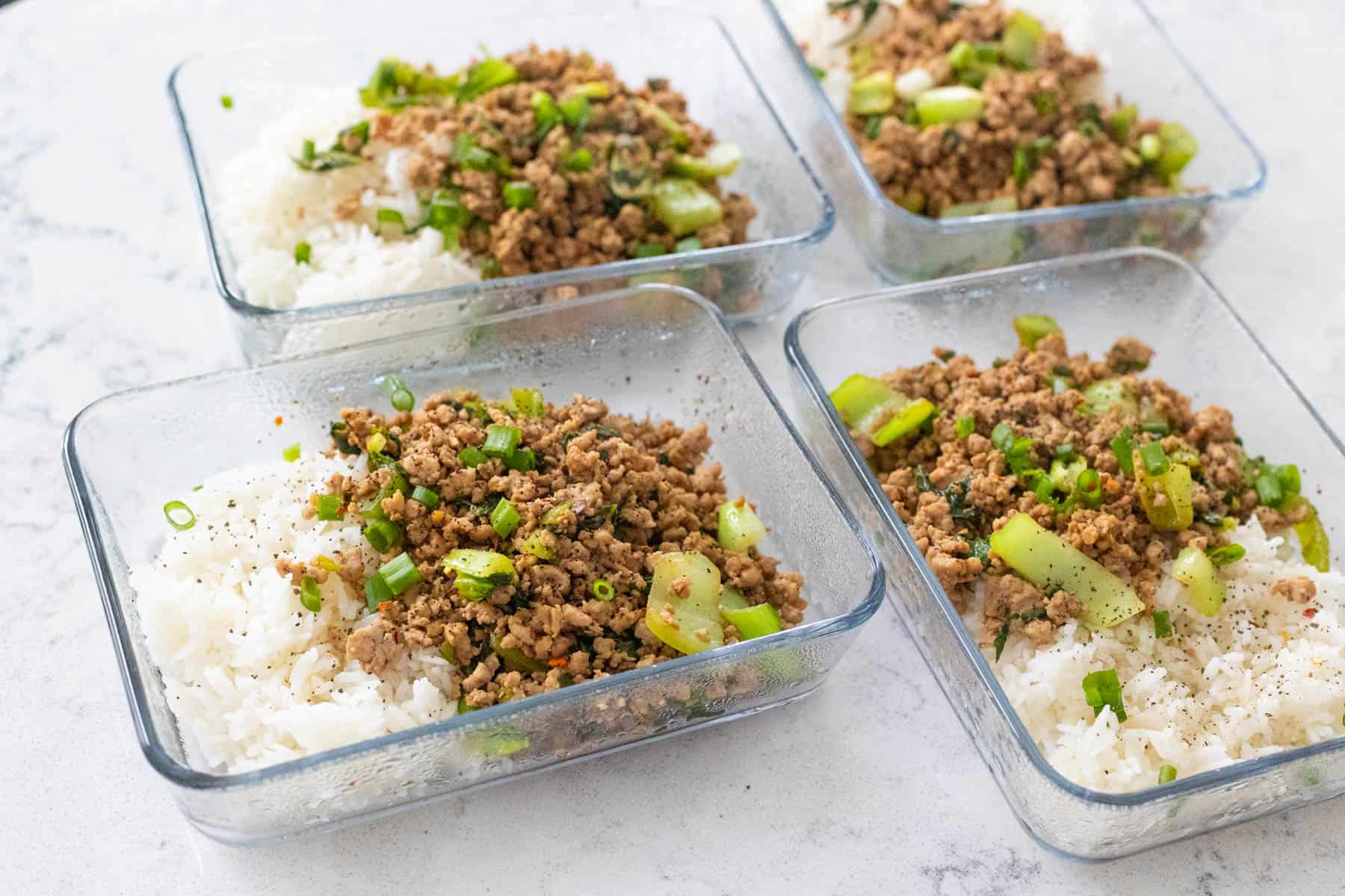 Four meal prep dishes are filled with beds of white rice topped with a ground pork and veggie mixture.