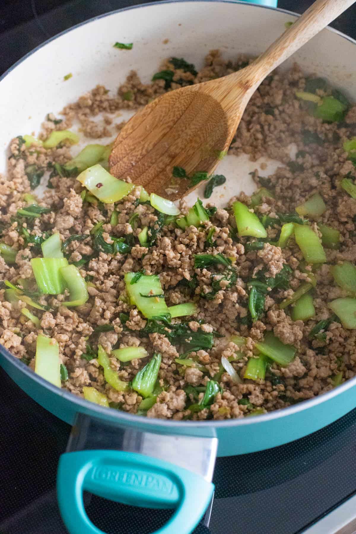 Ground pork cooked with chopped cabbage in a skillet, stirred with a wooden spoon as it finishes cooking for rice bowls with potsticker sauce.
