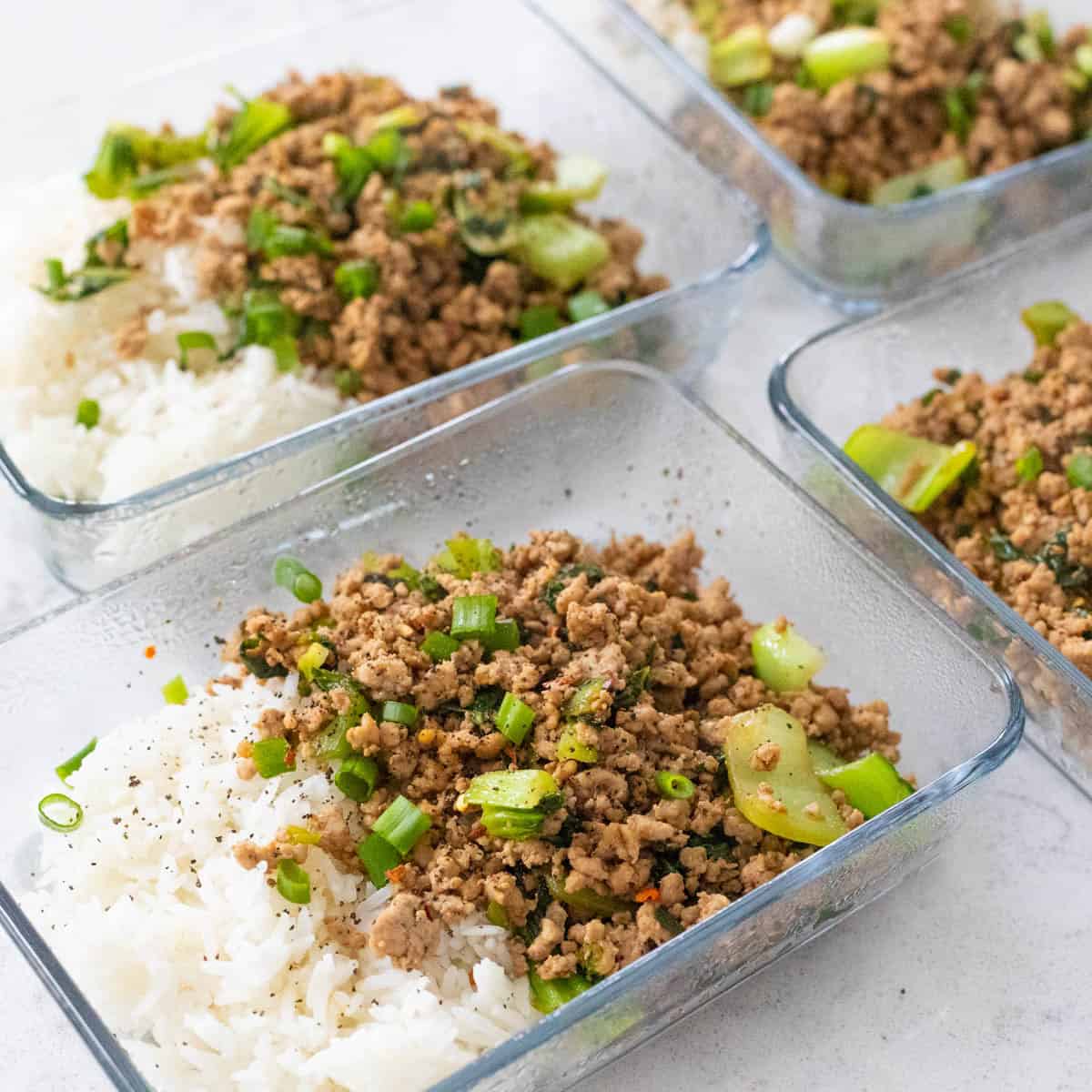 Four meal prep dishes are filled with beds of white rice topped with a ground pork and veggie mixture.