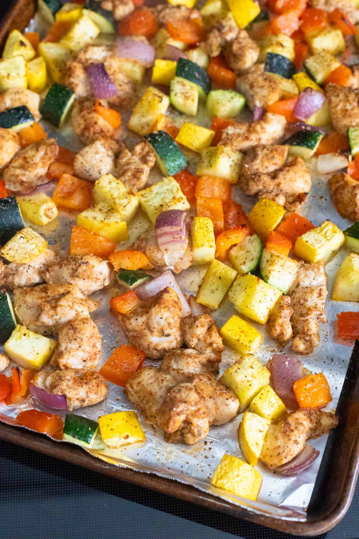 A sheet pan filled with tender chunks of seasoned chicken with chopped zucchini, peppers, and squash.