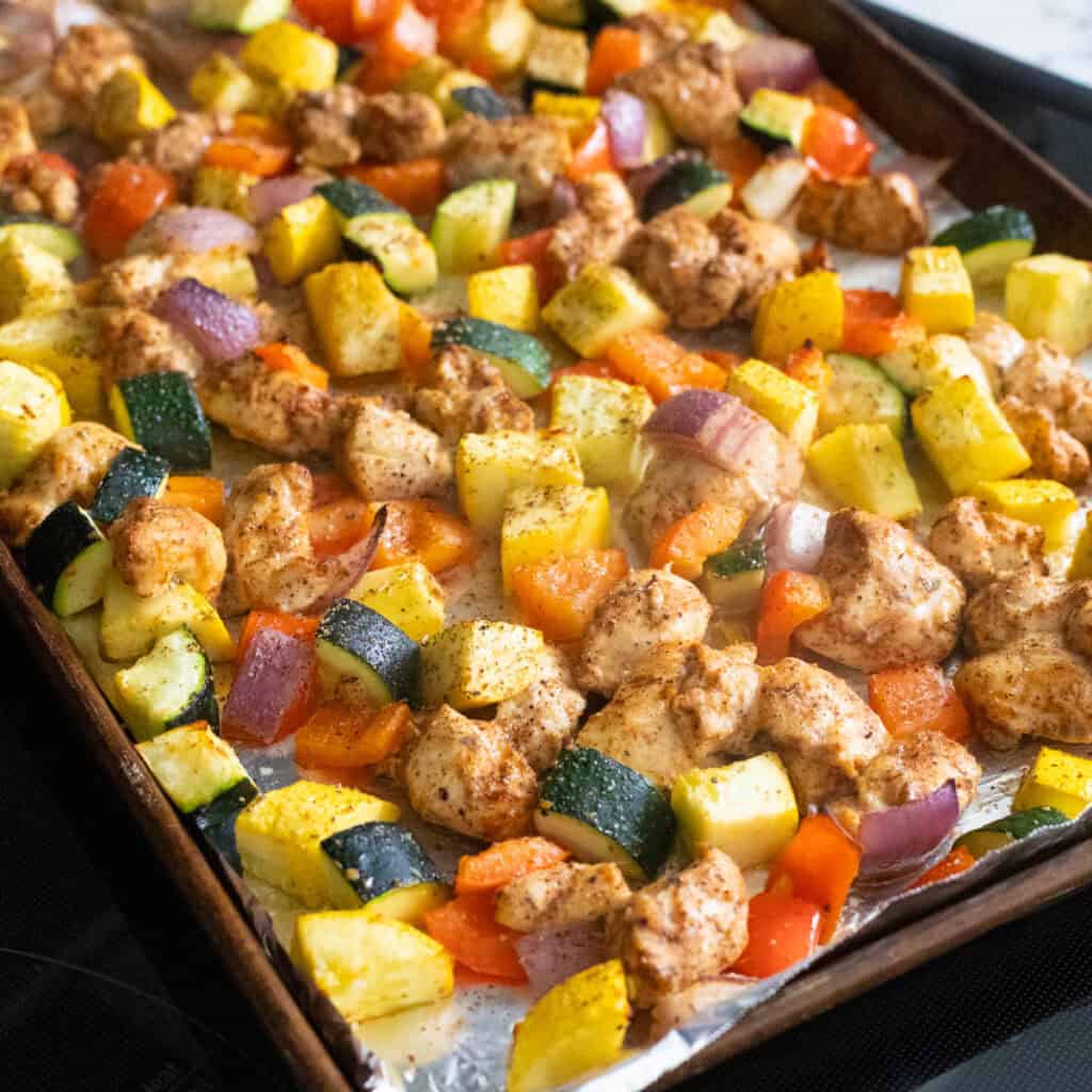 A sheet pan filled with tender chunks of seasoned chicken with chopped zucchini, peppers, and squash.