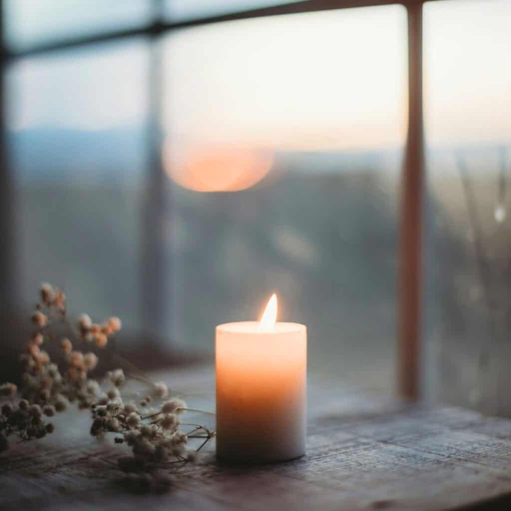 A single candle glows in the window of a serene view.