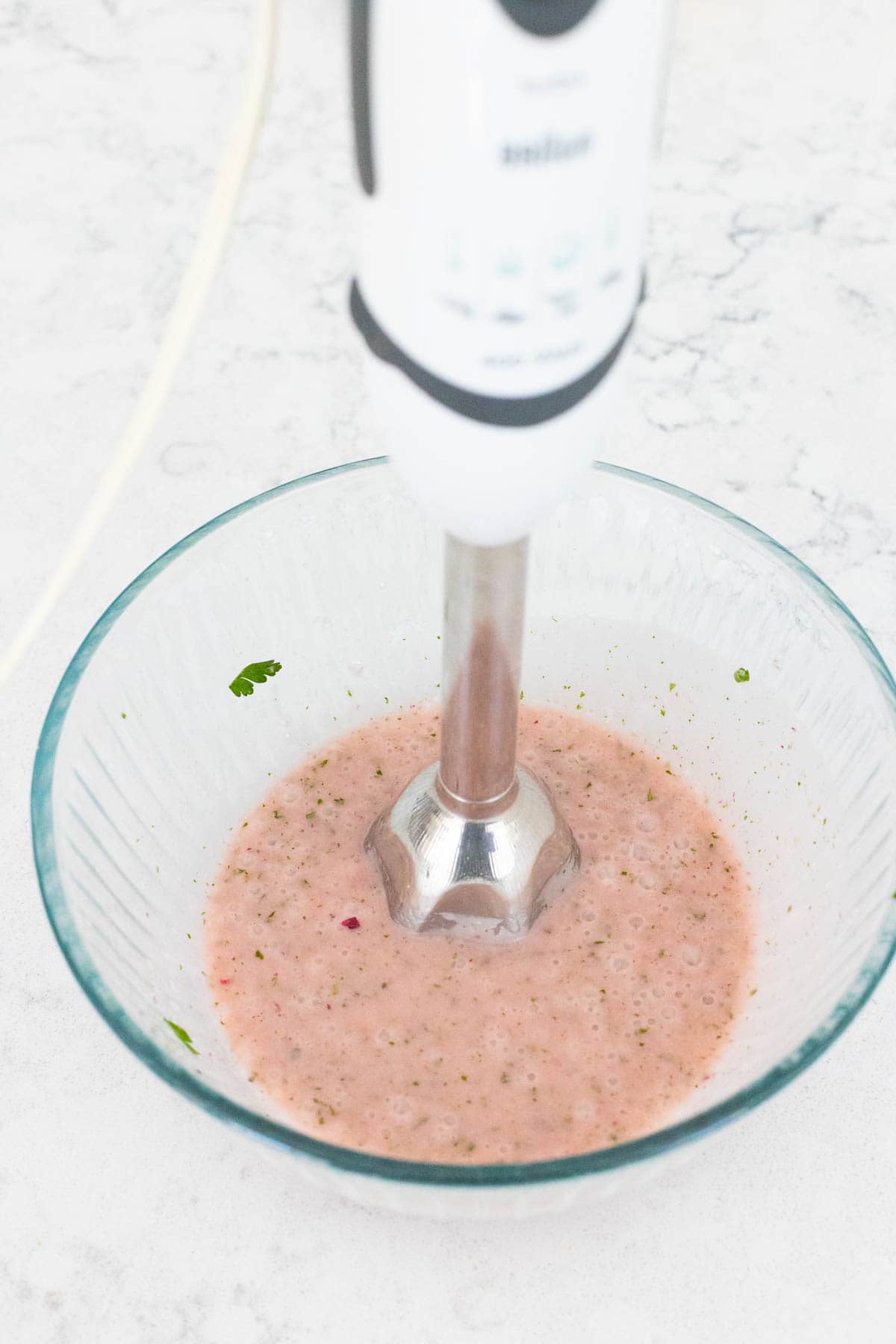 An immersion blender is mixing together the ingredients in the bowl.