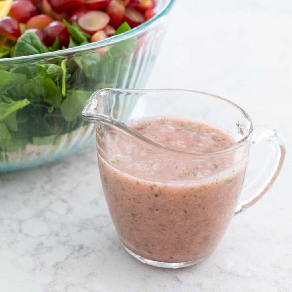 A small pitcher of the homemade onion vinaigrette sits next to a large bowl of salad.