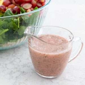 A small pitcher of the homemade onion vinaigrette sits next to a large bowl of salad.