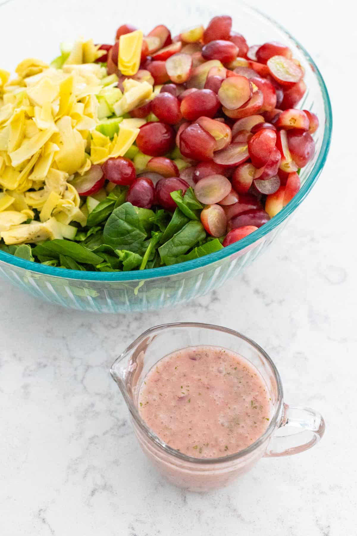 The pitcher of red onion vinaigrette is next to the salad bowl.