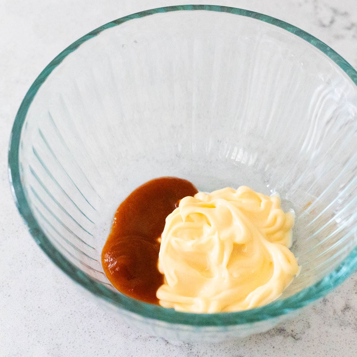 Mayonnaise and hot sauce combined in a glass bowl, ready to be mixed into spicy mayo.