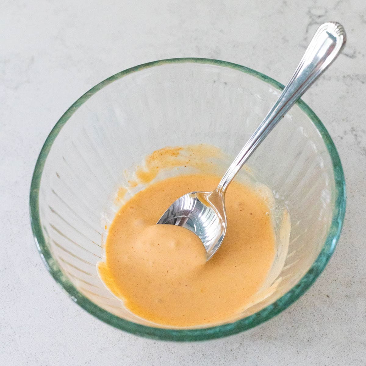 Smooth spicy mayo blended in a glass bowl with a spoon, ready to serve.
