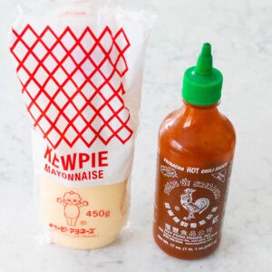A bottle of Kewpie mayo and a bottle of sriracha sauce are on the counter.