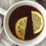 A cup of tea with two slices of lemon rests on a knit sweater.