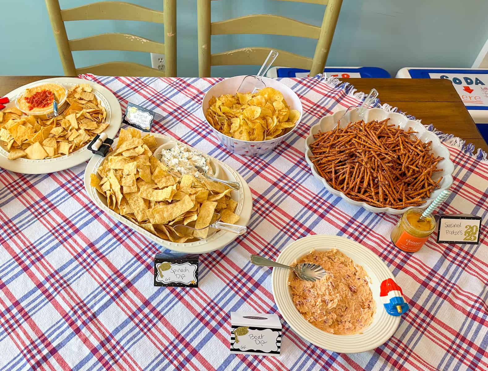 Trays of pretzels, chips, and dips in bowls are on the party table.