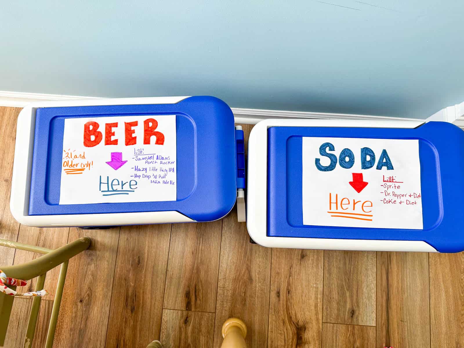 Two coolers filled with ice and beverages have hand drawn signs on top that say what is inside.